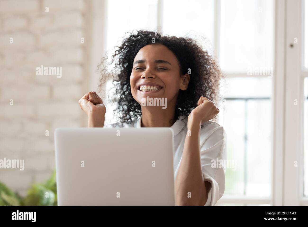 Un jeune employé africain souriant et souriant célébrant le succès en ligne. Banque D'Images