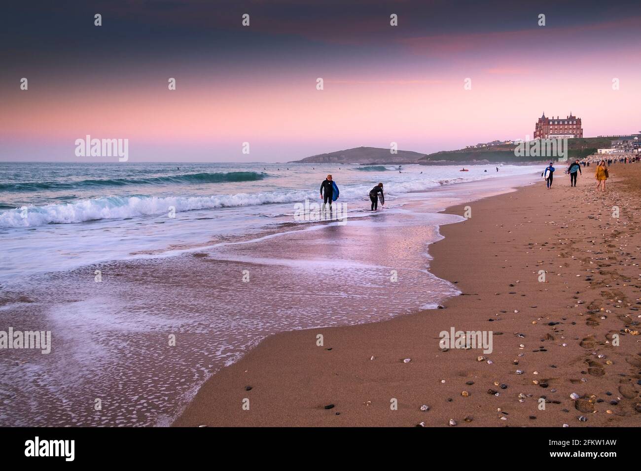 Coucher de soleil sur les surfeurs marchant dans la mer à Fistral Beach à Newquay dans les Cornouailles. Banque D'Images