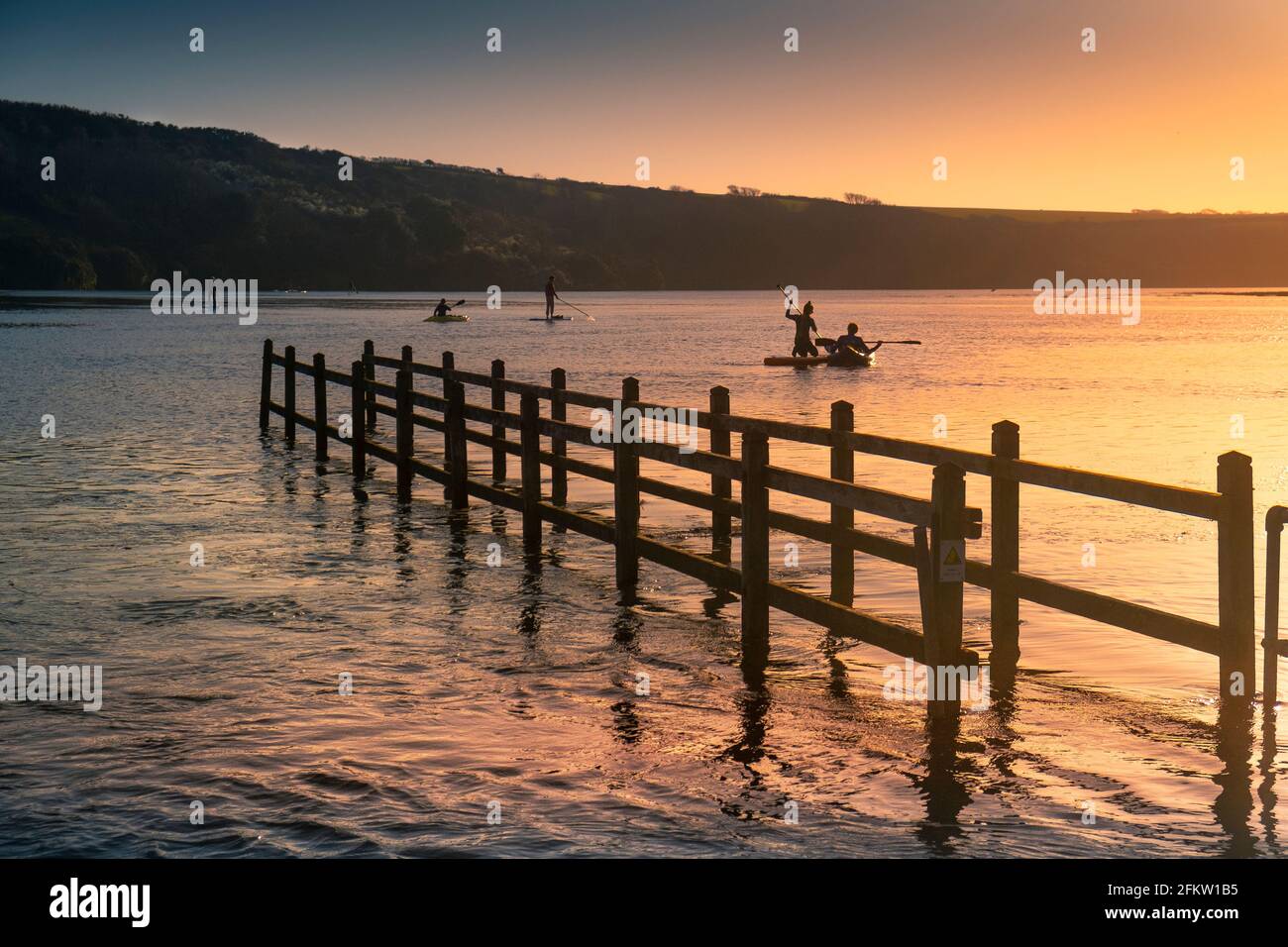 Coucher de soleil doré sur les personnes pagayant des kayaks et stand Up Paddleboard sur la rivière Gannel à marée haute à Newquay dans les Cornouailles. Banque D'Images