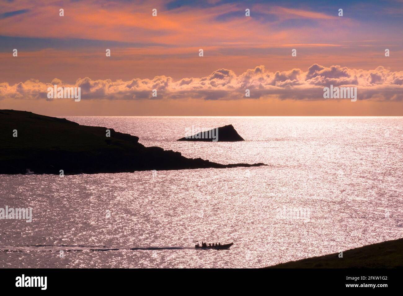 Un bateau à moteur touristique naviguant au-delà de Pentire point West et Le Chick une île rocheuse inhabitée silhouettée par un coloré Coucher de soleil à Newquay à Cornwal Banque D'Images