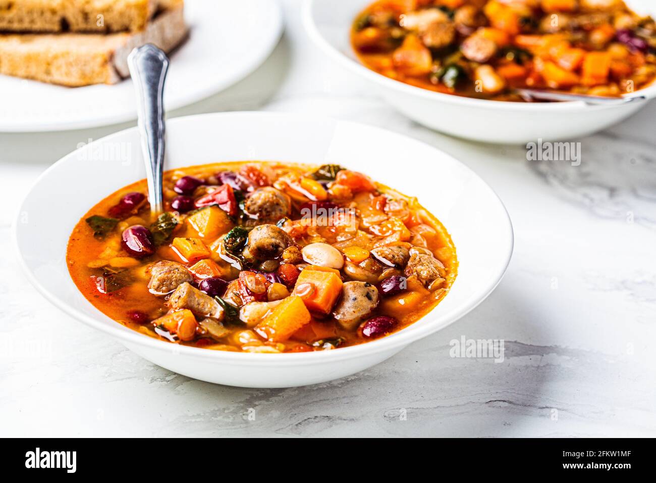 Soupe de haricots avec saucisses dans une assiette blanche, fond en marbre blanc. Concept de cuisine italienne. Banque D'Images