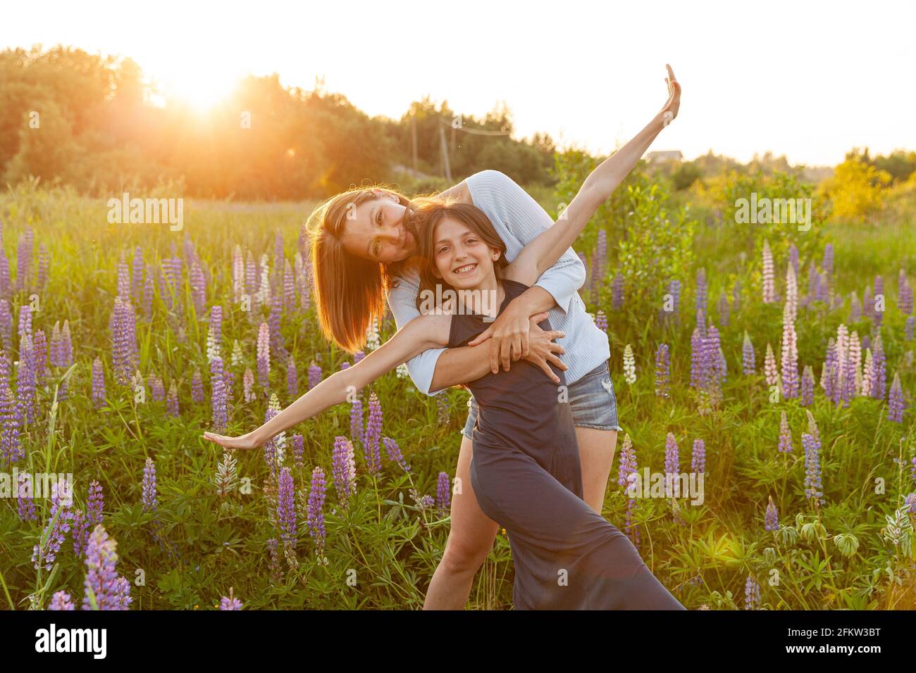 Jeune mère embrassant son enfant à l'extérieur. Femme et adolescente sur le terrain d'été avec fleurs sauvages fleur de fond vert. Bonne famille maman et dau Banque D'Images