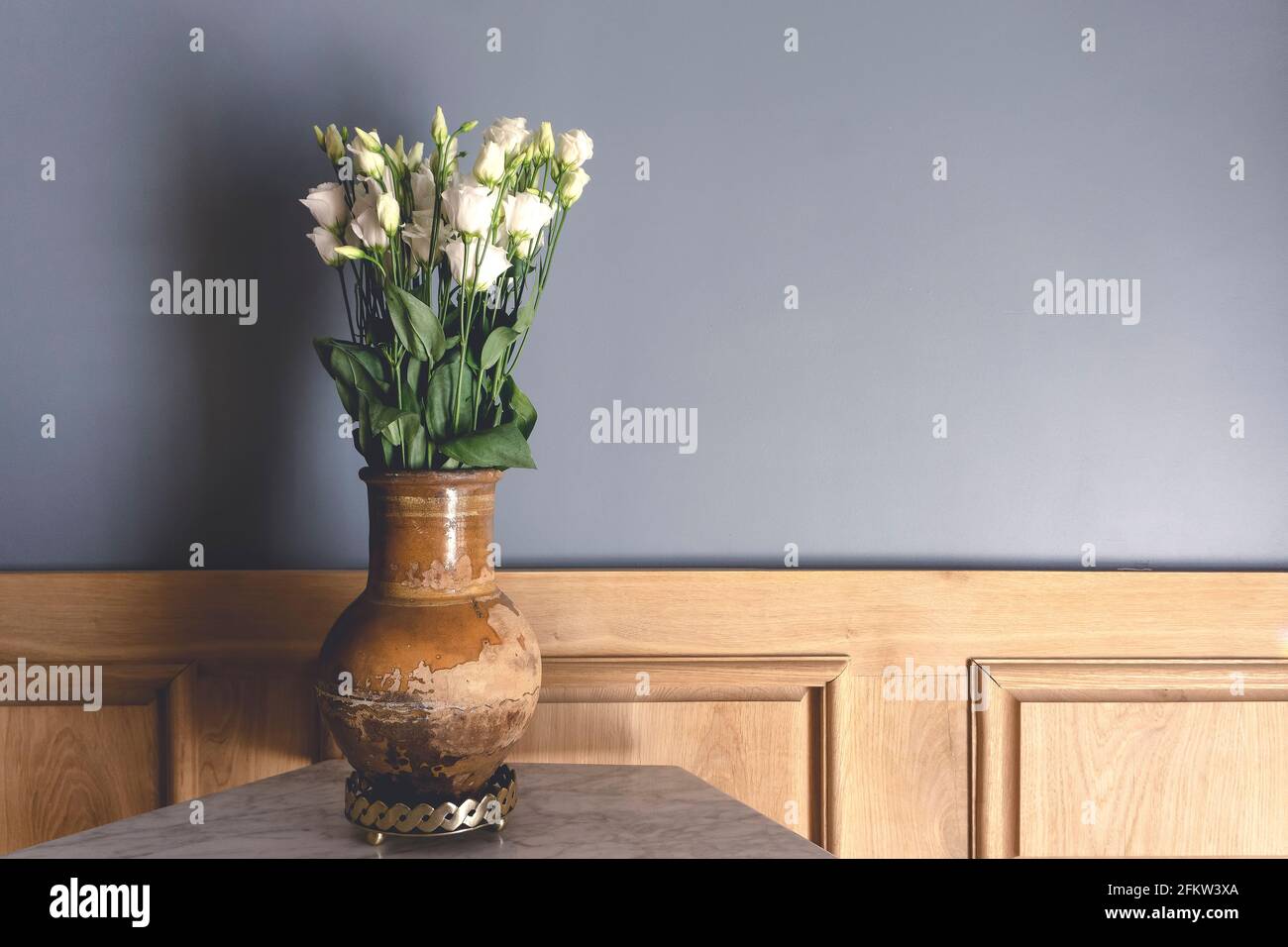 Chambre de style rétro. Vieux vase en argile avec fleurs blanches roses sur le fond d'un mur gris vide. Intérieur vintage d'un salon de maison ancienne. Décoration ancienne et décoration intérieure. Photo de haute qualité Banque D'Images