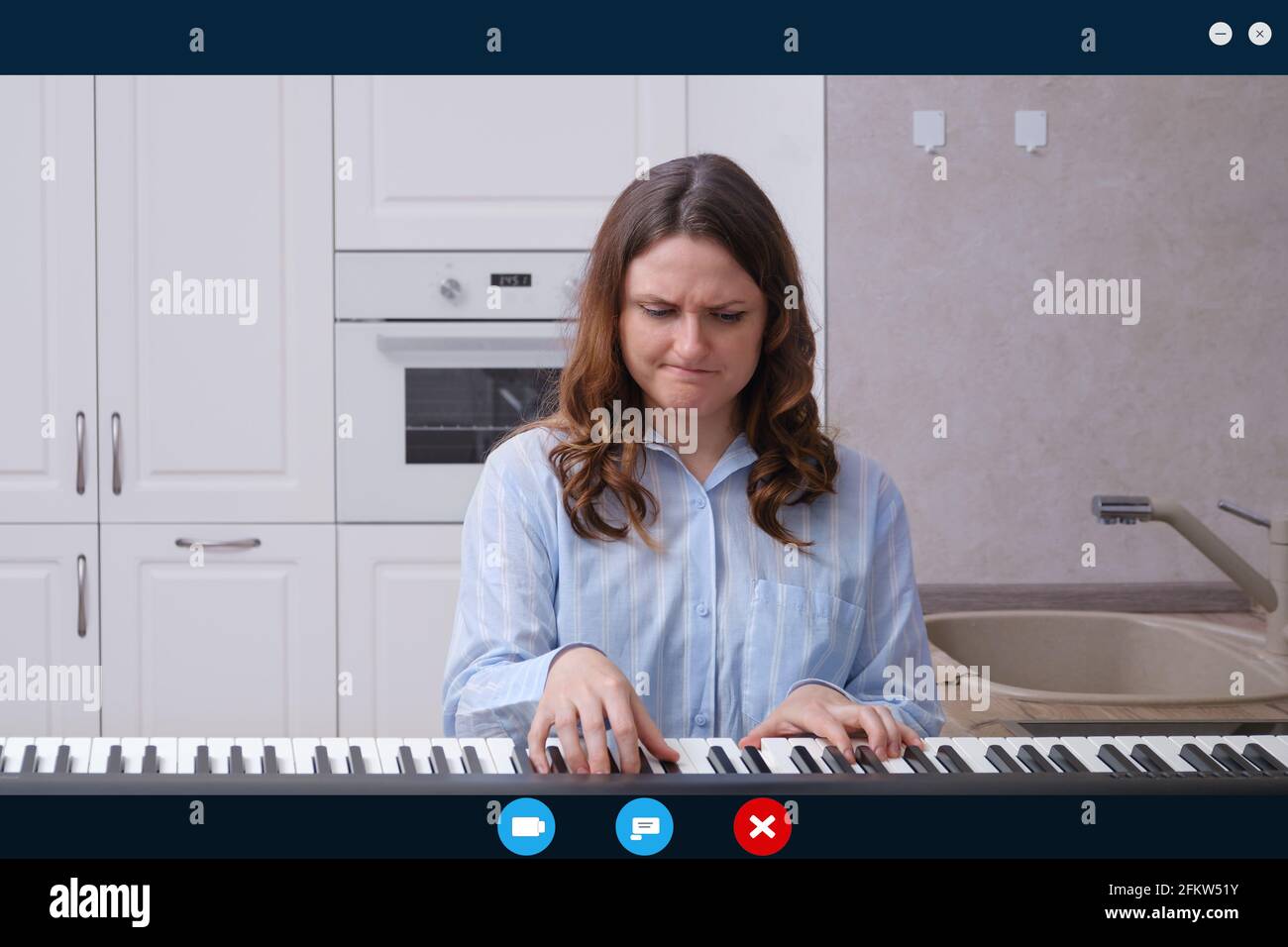 Angry Woman joue du piano tout en étant assise dans une cuisine à la maison  dans un chat vidéo en ligne. Écran avec interface de chat et d'appel vidéo  Photo Stock -