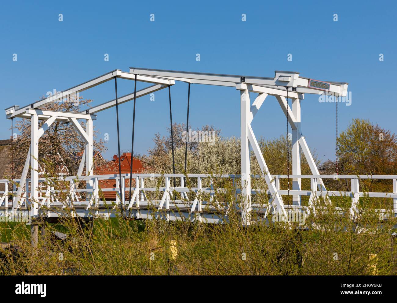 Pont de Hogendiekbrücke, pont en bois traversant la rivière Lühe dans la région d'Altes Land en Basse-Saxe, fleurissant des arbres en arrière-plan Banque D'Images