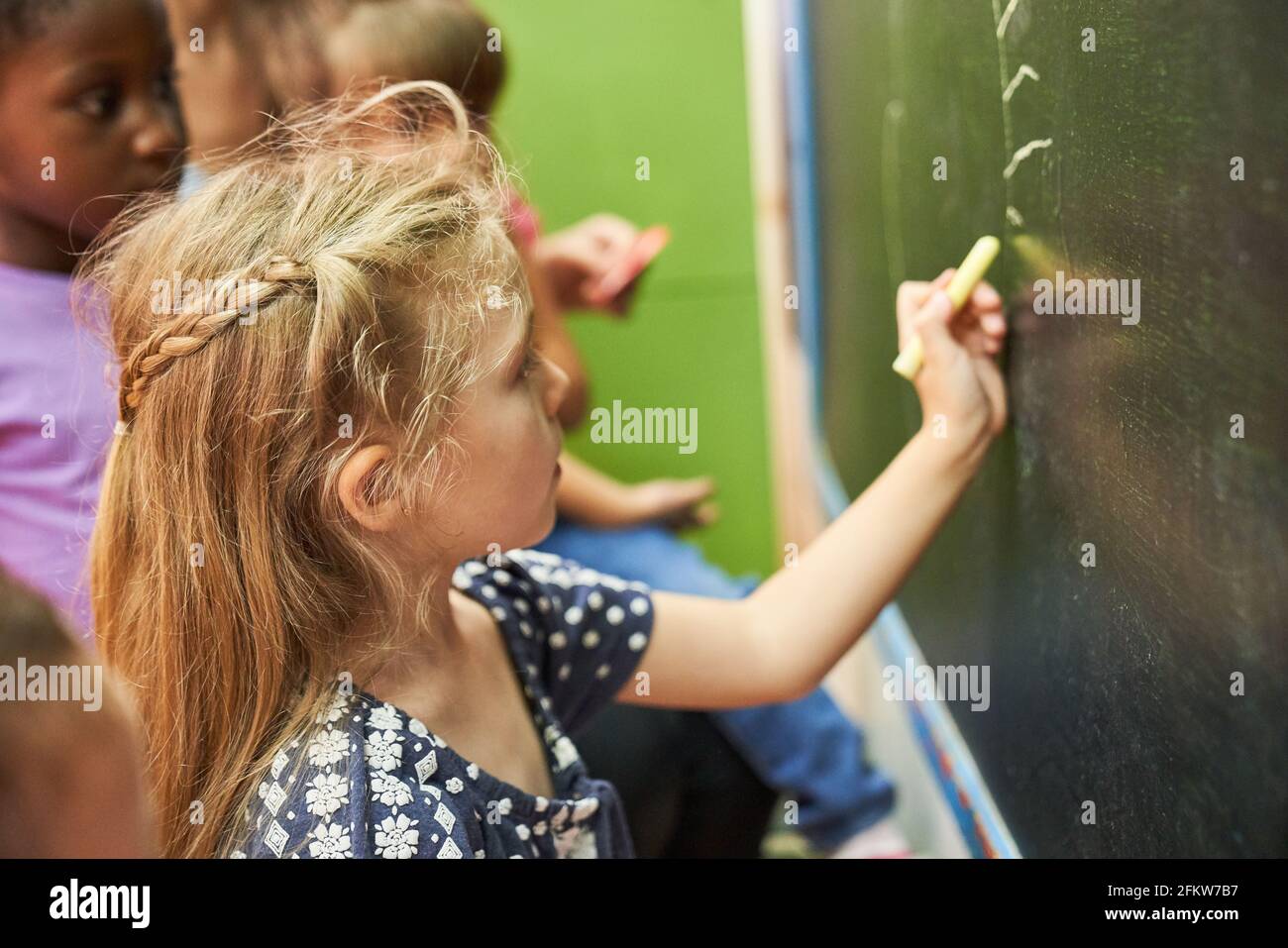 Une fille peint avec de la craie sur le tableau noir de l'école à la maternelle ou préscolaire Banque D'Images