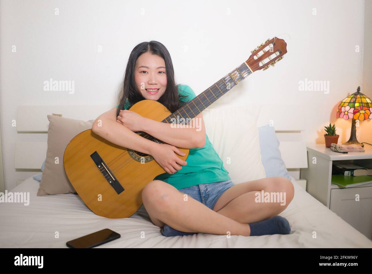 Jeune femme asiatique heureuse jouant de la guitare au lit - attrayante Et  belle fille chinoise dans la chambre à coucher appréciant le chant et  l'écriture musique détendue à la maison Photo