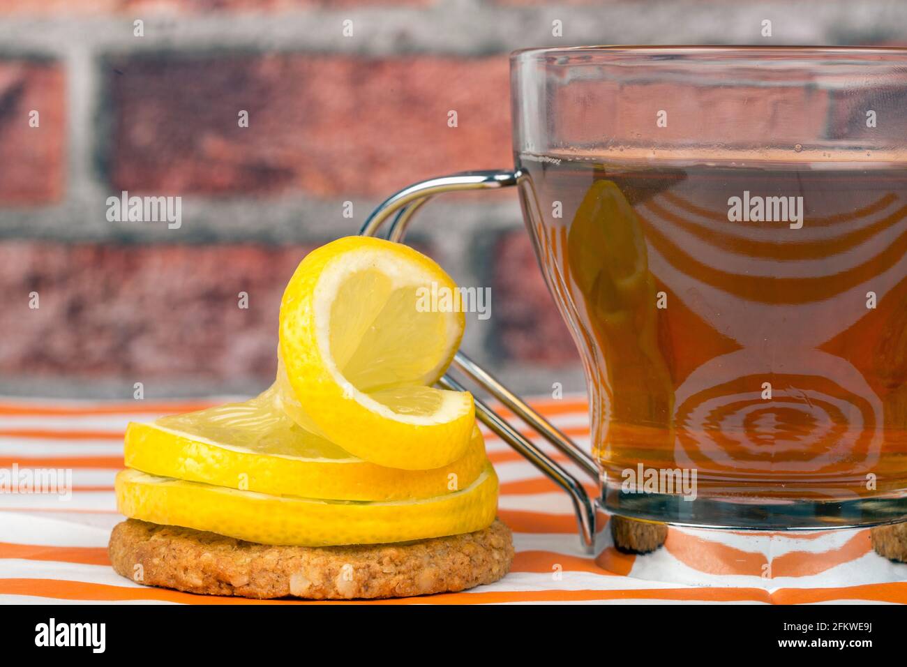 Tranches de citron placées de façon décorative sur un biscuit de flocons d'avoine et un verre avec thé sur fond de mur de brique Banque D'Images