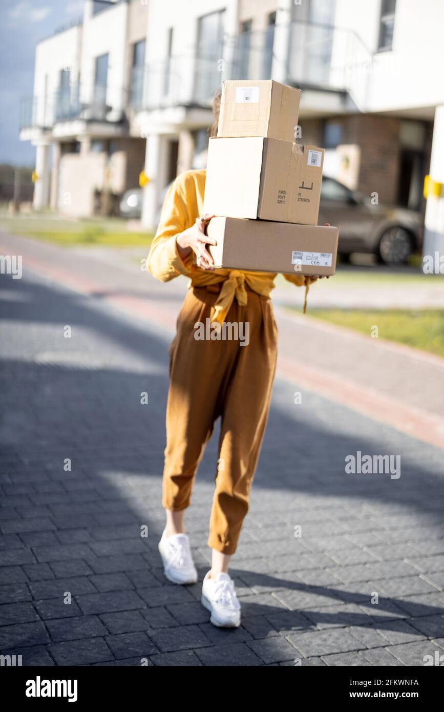 Femme tenant des colis dans la rue en face de la maison. Réception des marchandises commandées au bureau de poste. Achats en ligne. Service de livraison. Banque D'Images