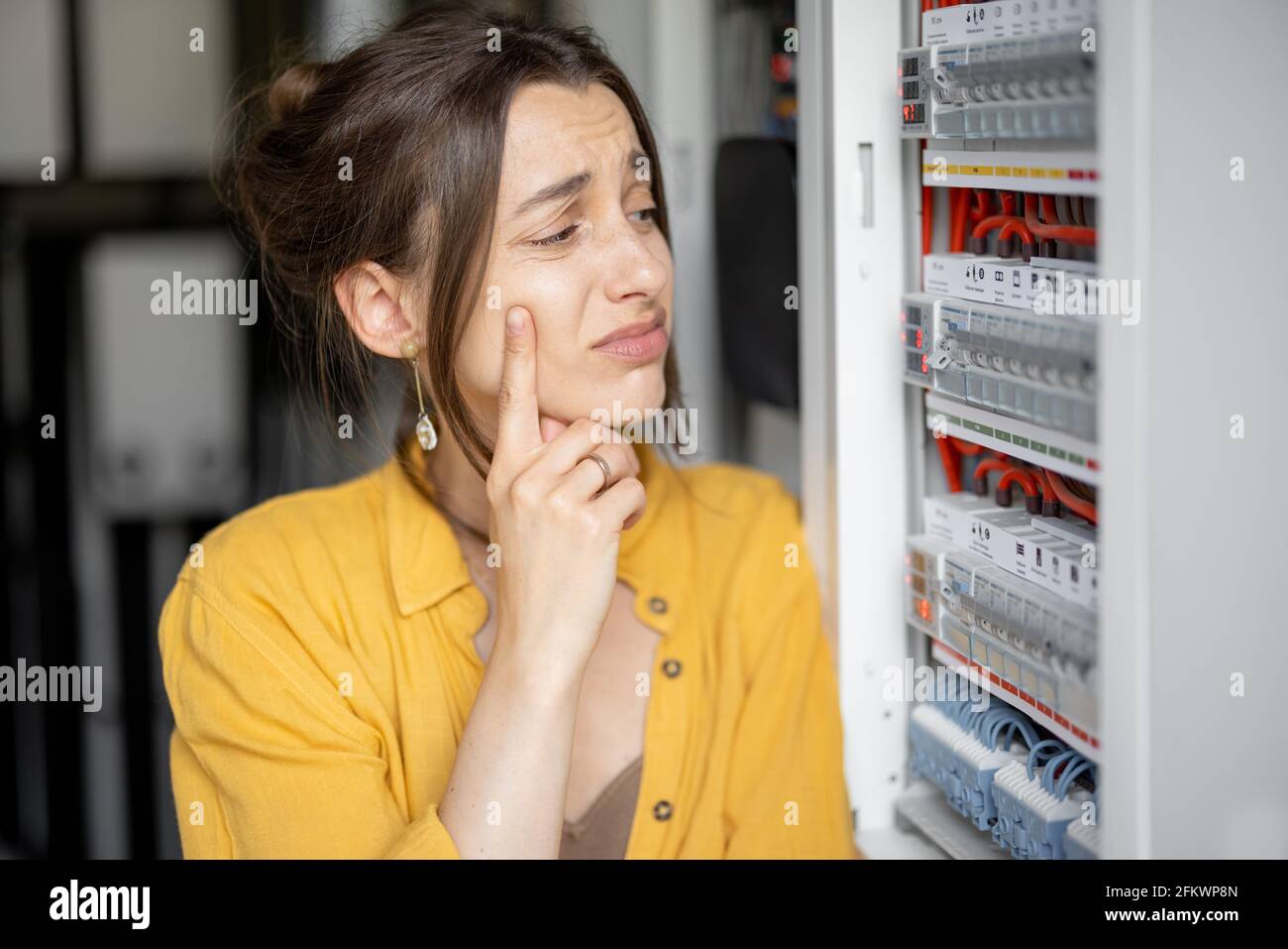 Femme confuse ayant des problèmes avec l'électricité à la maison, parle au téléphone essayant de résoudre le problème. Concept de l'incompétence des femmes dans l'électricité domestique Banque D'Images