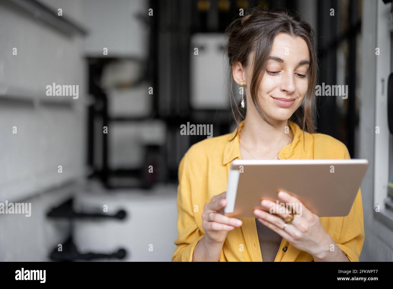 La jeune femme au foyer surveille les performances des dépenses domestiques sur une tablette numérique, debout dans la chaufferie à la maison Banque D'Images