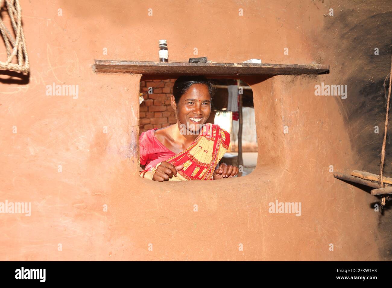 Femme souriant de la fenêtre de la maison de boue. LA TRIBU DESIA KONDHA. Village de Goipeta, Odisha, Inde. Visages de l'Inde rurale Banque D'Images