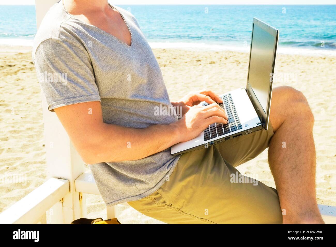 Mettre en place un jeune homme en utilisant un ordinateur portable assis sur une véranda de plage en bois blanc. Concept freelance. Programmateur mâle fonctionnant sur ordinateur portable, sc vierge Banque D'Images