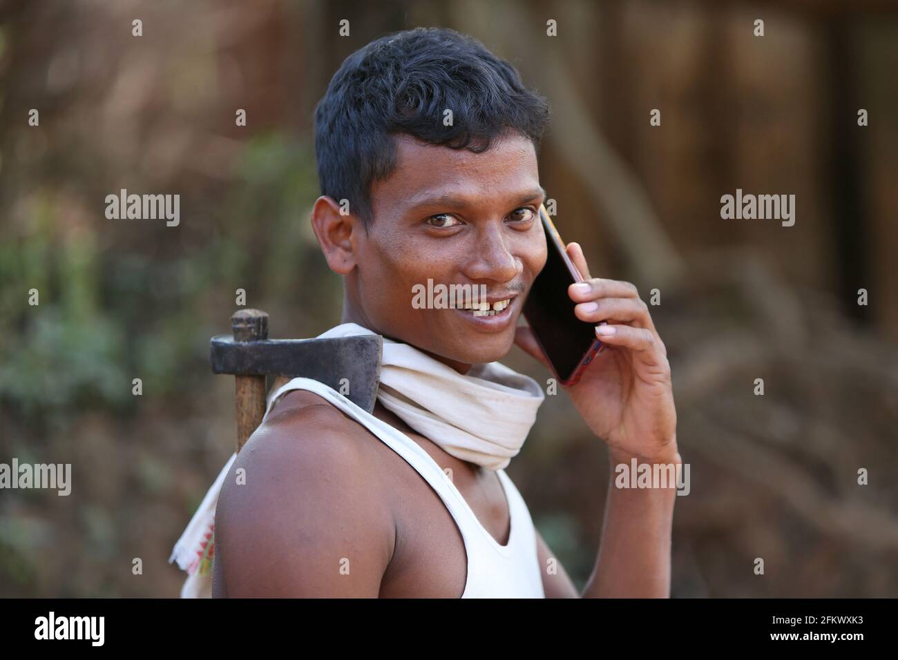 Fermier tribal mâle avec hache sur l'épaule parlant sur téléphone portable au village de Lanjigadh à Odisha, Inde. LA TRIBU DESIA KONDHA. Visages de l'Inde rurale Banque D'Images