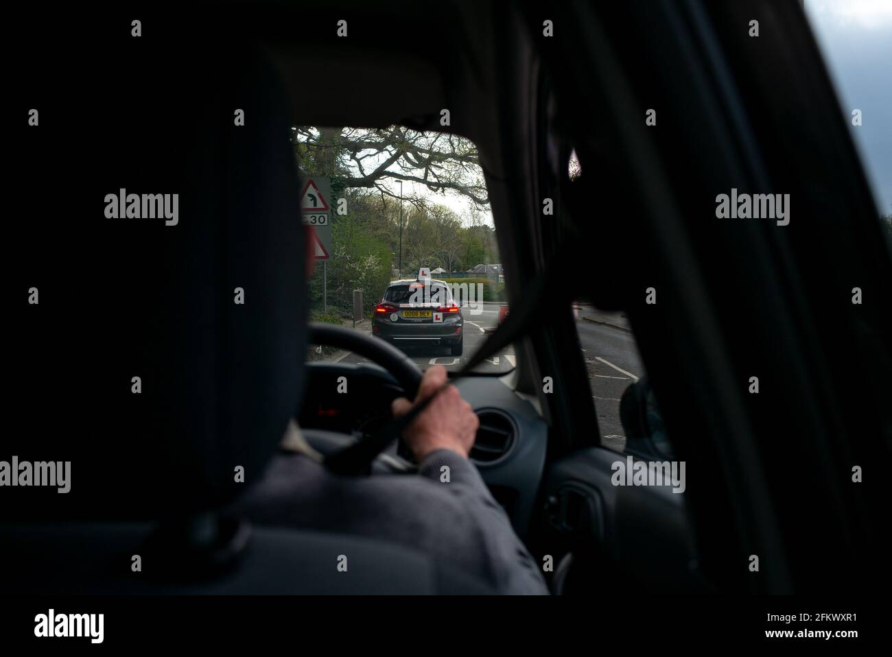 Un automobiliste âgé qui suit un conducteur apprenant vu depuis le siège arrière derrière le conducteur. Banque D'Images