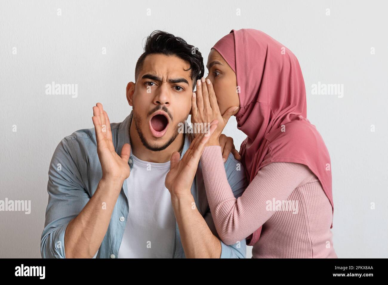 Partage du secret. Musulmane dame dans le hijab commérages avec son mari choqué Banque D'Images