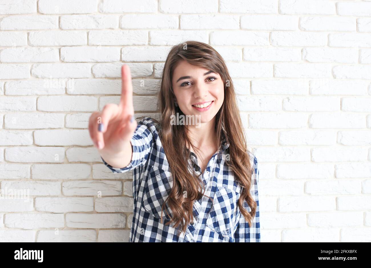 Belle jeune femme touchant le concept de bouton d'écran virtuel. Magnifique femme millénaire à yeux bruns avec de longs cheveux foncés ondulés et des dents et des caractères parfaits Banque D'Images