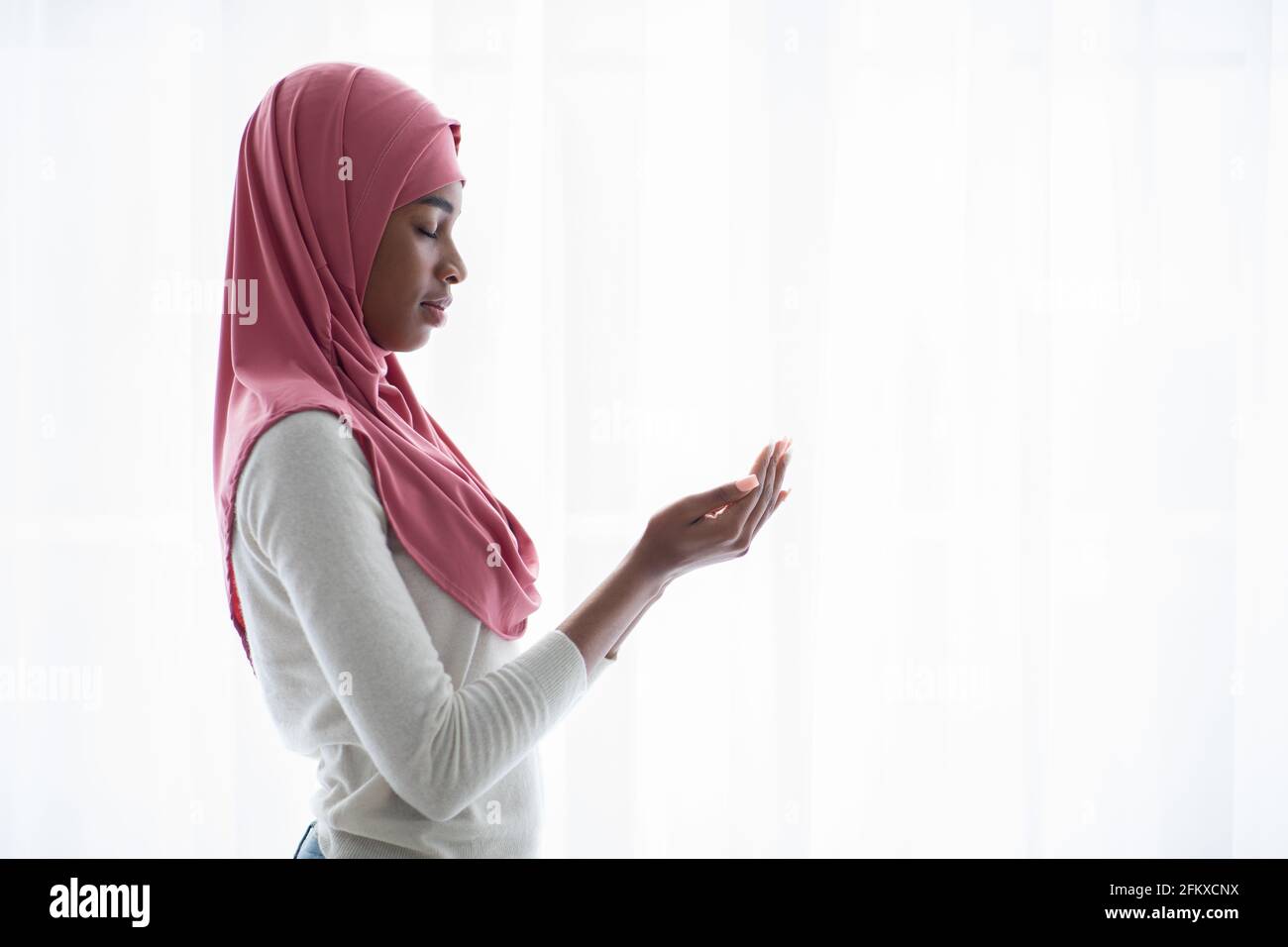 Portrait d'une jeune femme musulmane noire priant près de la fenêtre à accueil Banque D'Images