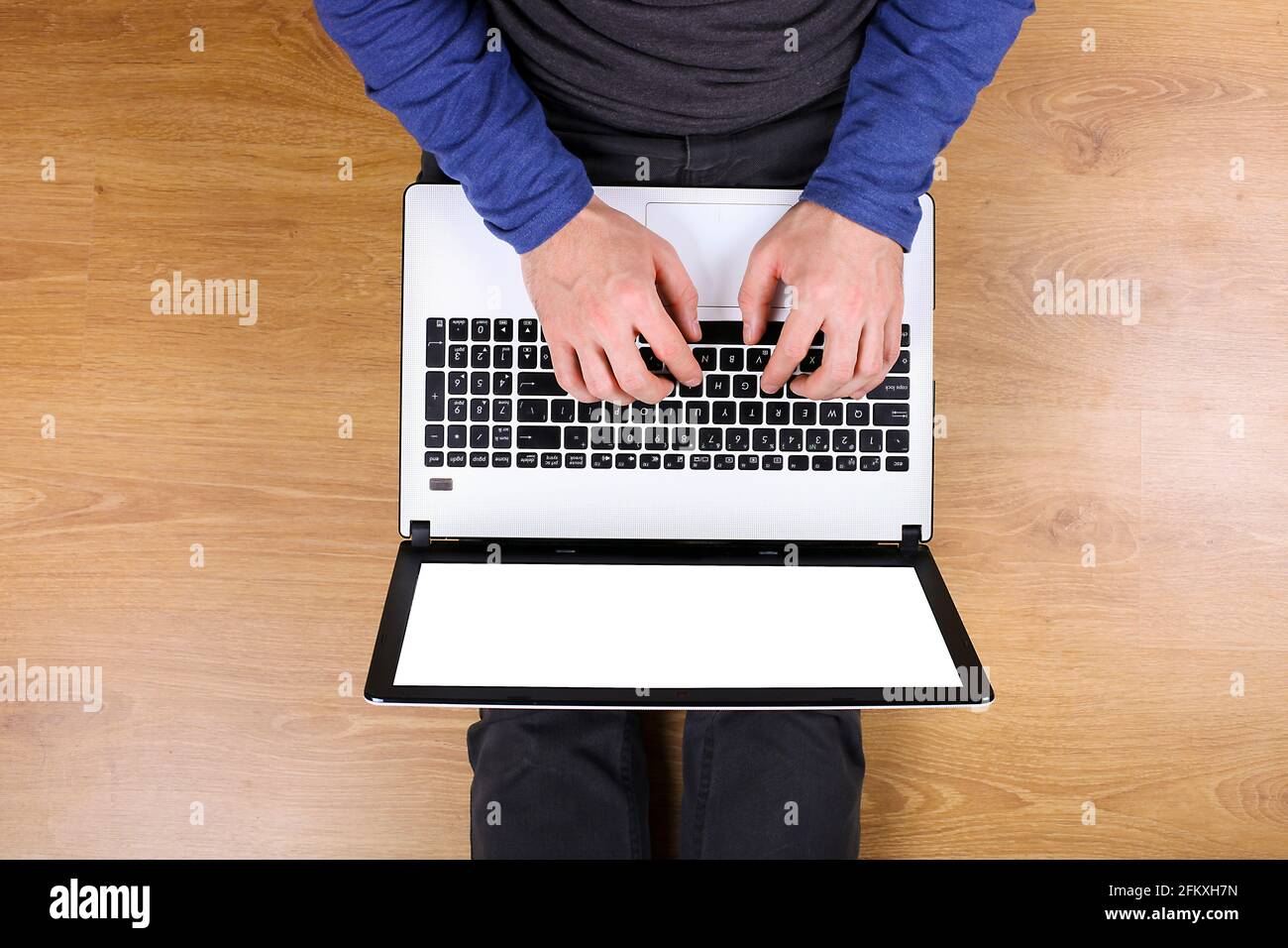 Vue de dessus, jeune homme avec ordinateur portable pc et téléphone portable sur ses genoux, assis sur fond de parquet. Vue aérienne des mains mâles sur le clavier, holdi Banque D'Images