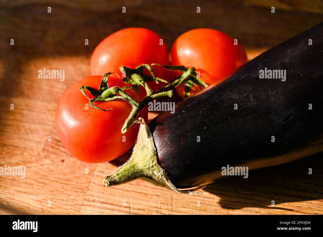 Tomates sur la vigne et une aubergine fraîche (aubergine) Solanum melongena sur une planche à découper en bois Banque D'Images