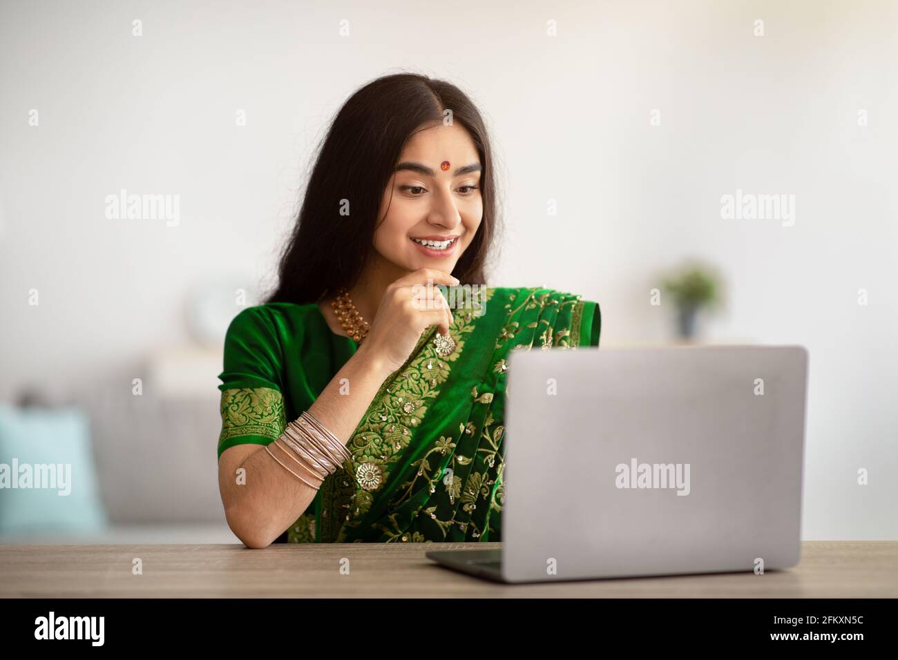 Jeune femme indienne dans la belle robe sari étudiant ou travaillant en ligne sur ordinateur portable, à l'intérieur Banque D'Images