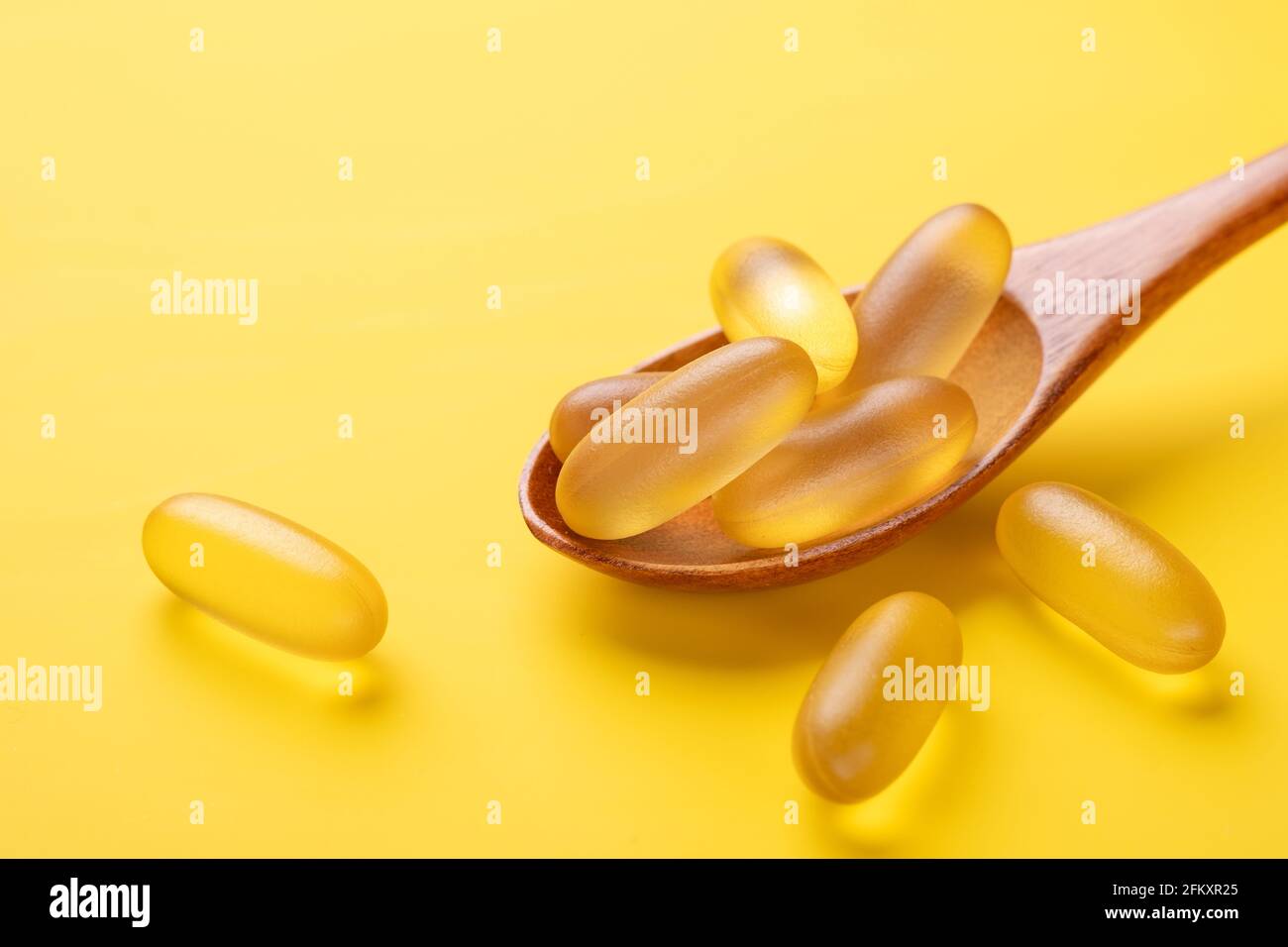 Fermez les capsules Omega 3 dans une cuillère en bois sur fond jaune. Gels à base d'huile de poisson. Compléments alimentaires en capsules de vitamine D. Espace de copie - image Banque D'Images