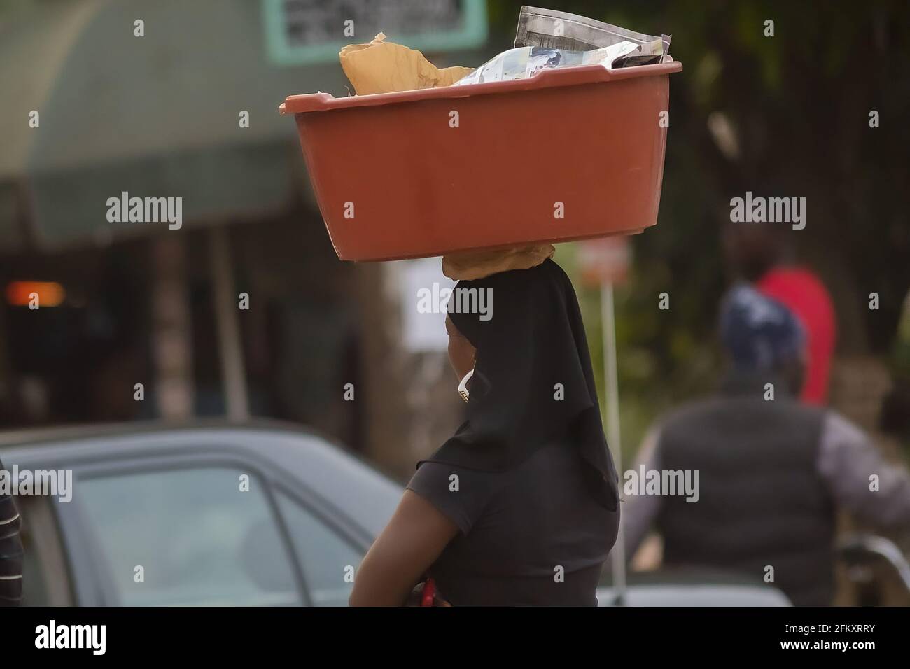 Femme africaine avec un anneau d'oreille portant un panier en plastique sur sa tête dans la ville de Yaoundé, Cameroun Banque D'Images