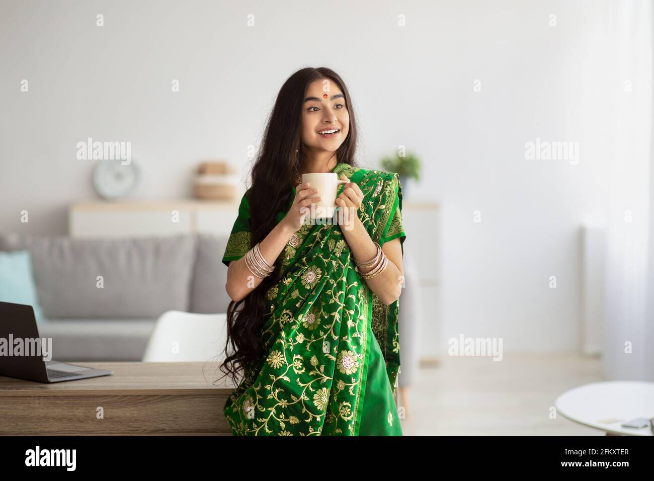 Jolie jeune femme indienne en robe verte sari ayant le café pause à la maison Banque D'Images