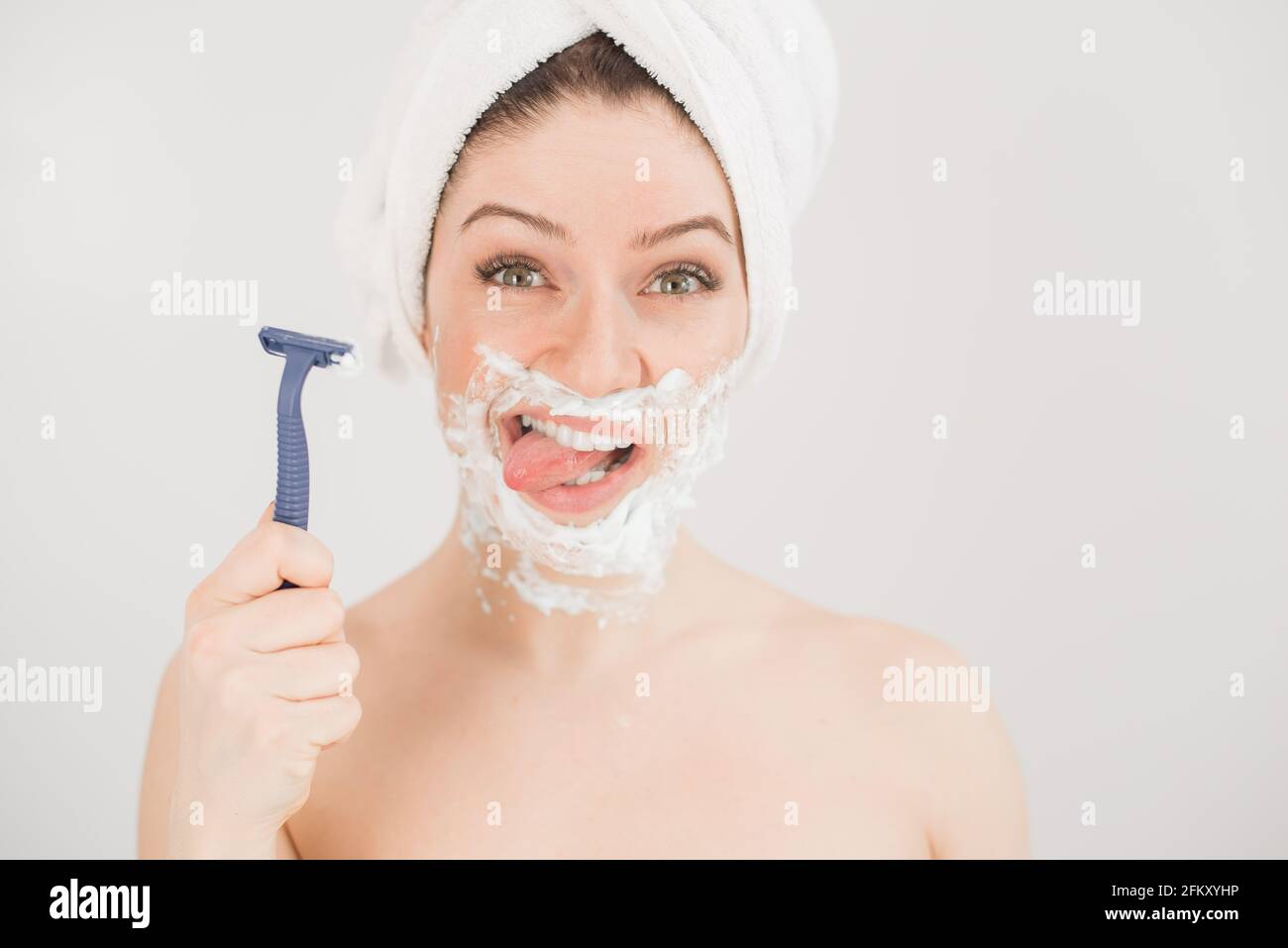 Portrait amusant d'une femme avec de la mousse à raser sur son visage  tenant un rasoir sur un fond blanc. La jeune fille enlève la moustache et la  barbe Photo Stock -