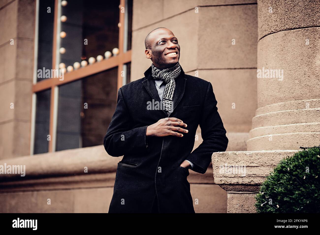 Portrait du jeune homme afro-américain souriant en Europe. Homme portant un manteau  noir, et se tenant près de l'ancienne architecture Photo Stock - Alamy