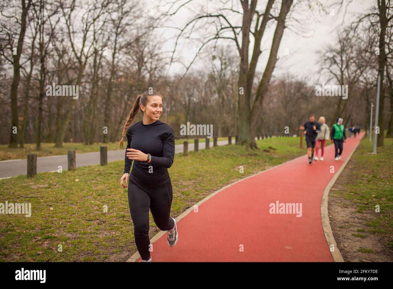 Une jeune femme, jogging à l'extérieur en automne, sur une piste. Les gens en arrière-plan. Banque D'Images