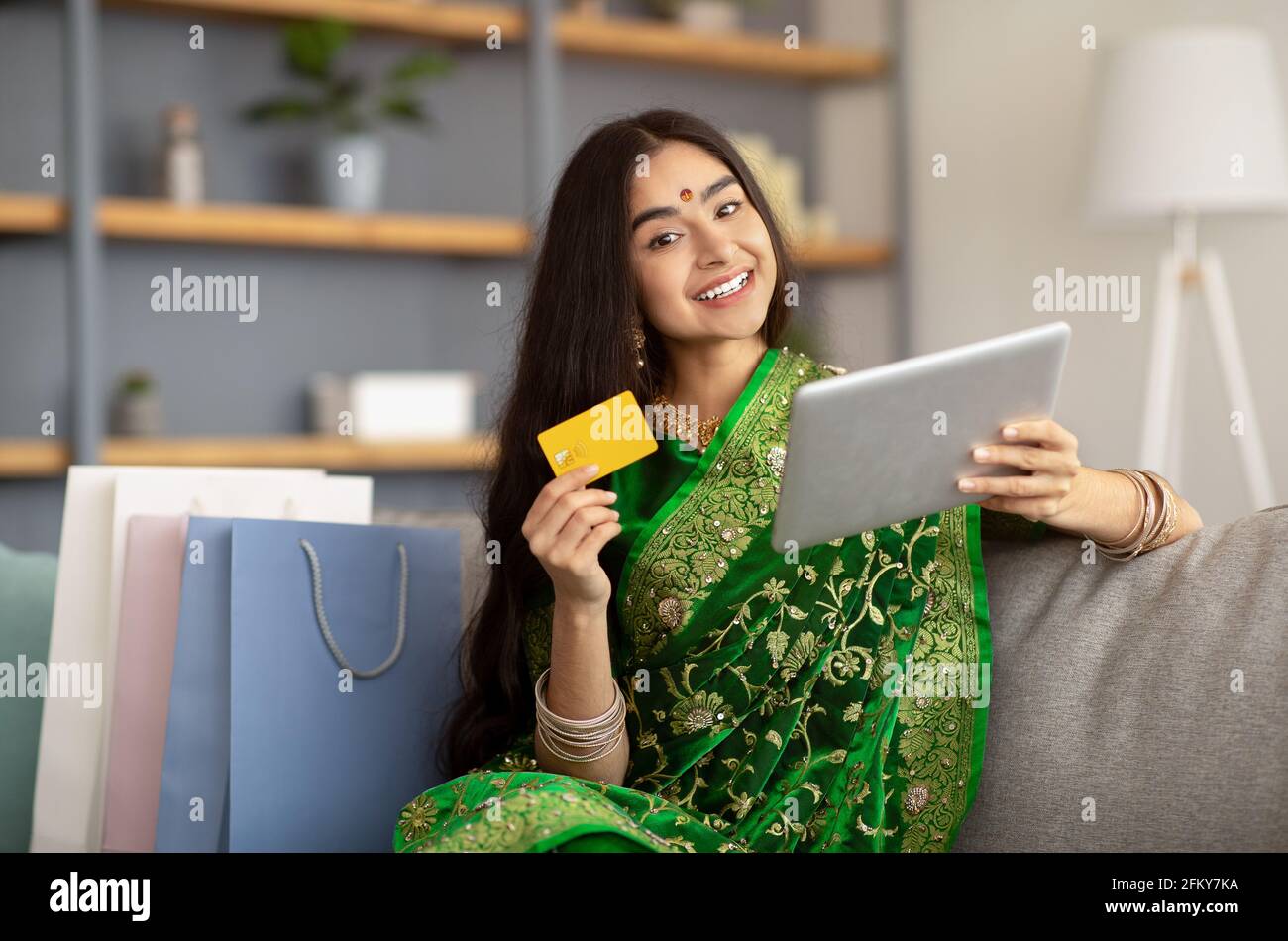 Femme indienne attrayante en robe ethnique sari utilisant une carte de crédit et une tablette pour les achats en ligne à la maison Banque D'Images