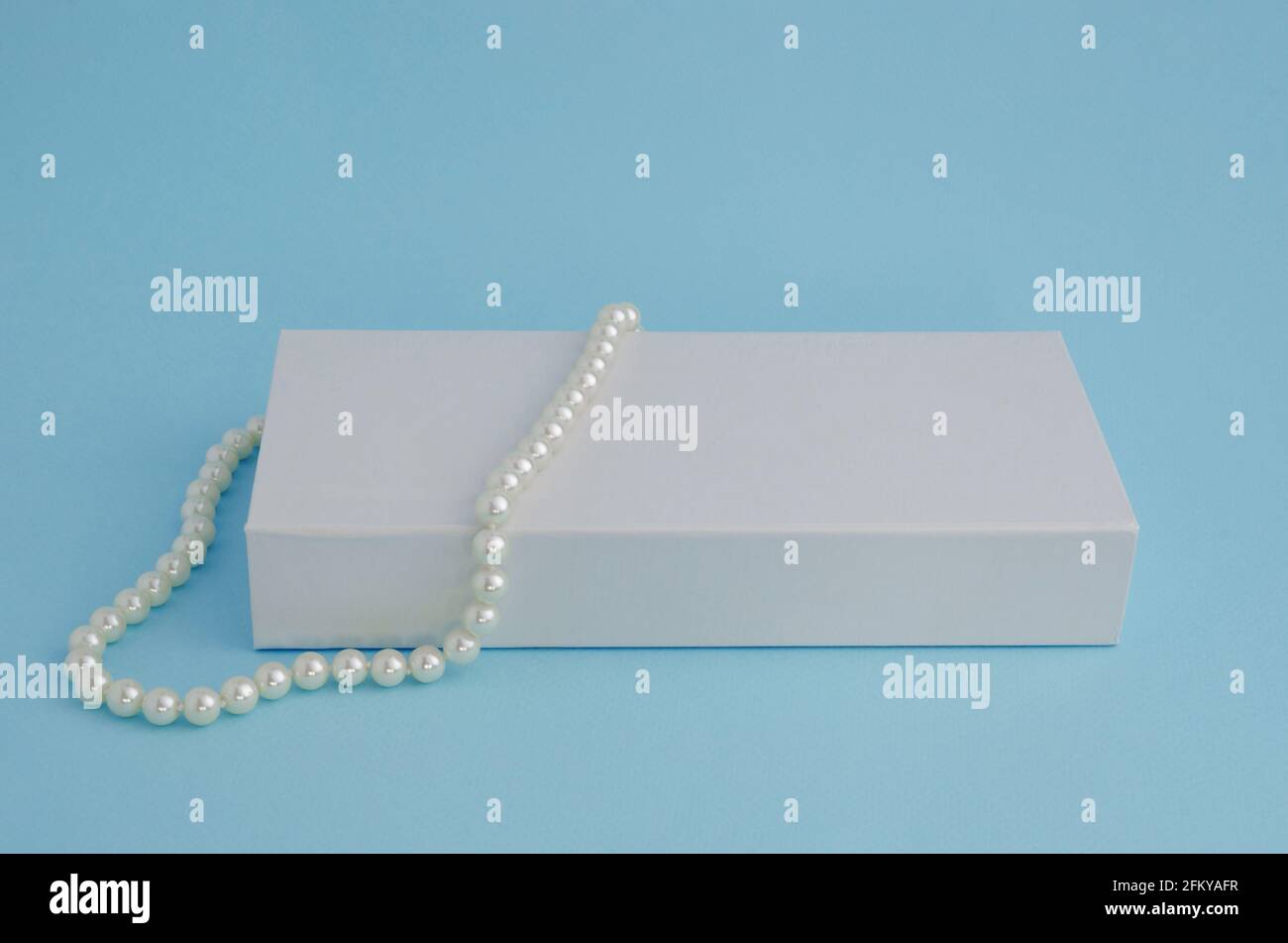 Une belle chaîne de collier de perles sur une boîte blanche sur un fond bleu. Banque D'Images