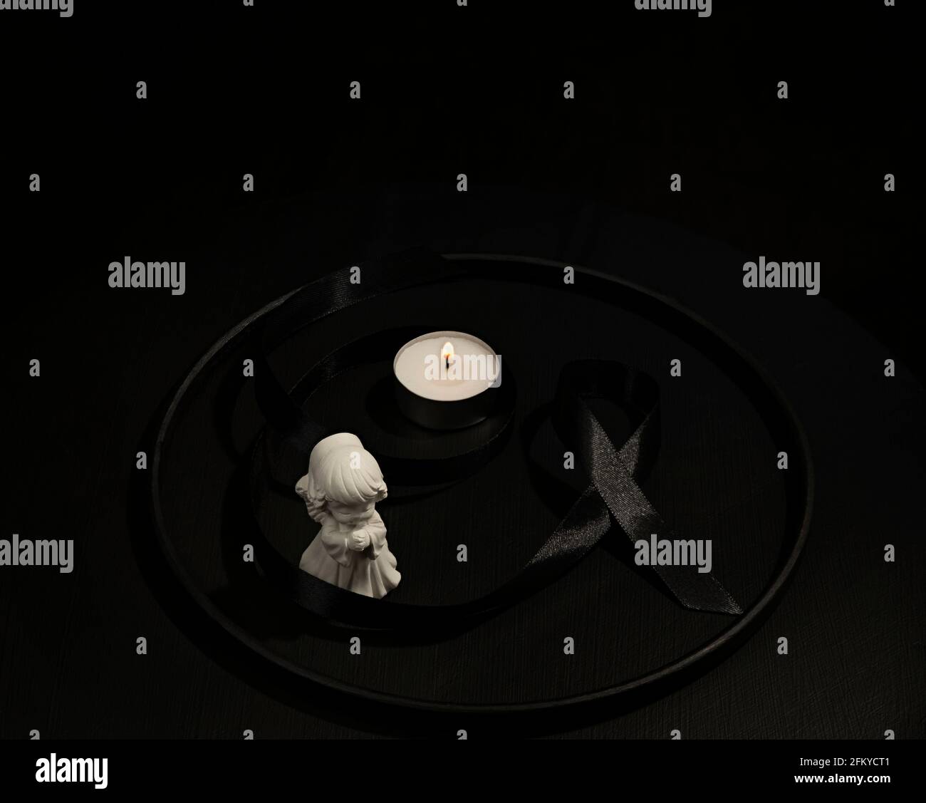 Ange blanc, ruban de deuil noir et bougie en cercle sombre image funéraire conceptuelle Banque D'Images