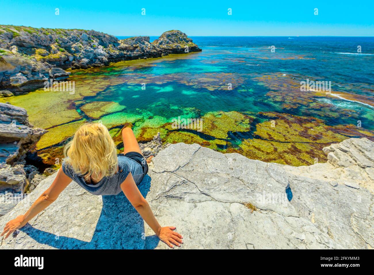 Une jeune fille touristique caucasienne fait du soleil sur des rochers qui regardent les eaux turquoise de Jeannies Lookout à Rottnest Island, Perth, Australie occidentale. Vue panoramique Banque D'Images
