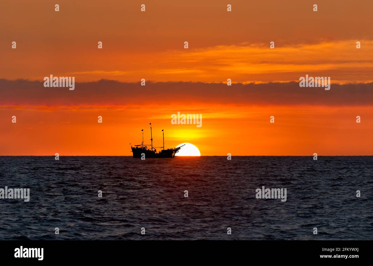 Un Pirate Ship se trouve sur l'océan, détouré contre UN Ciel coloré de coucher de soleil orange Banque D'Images