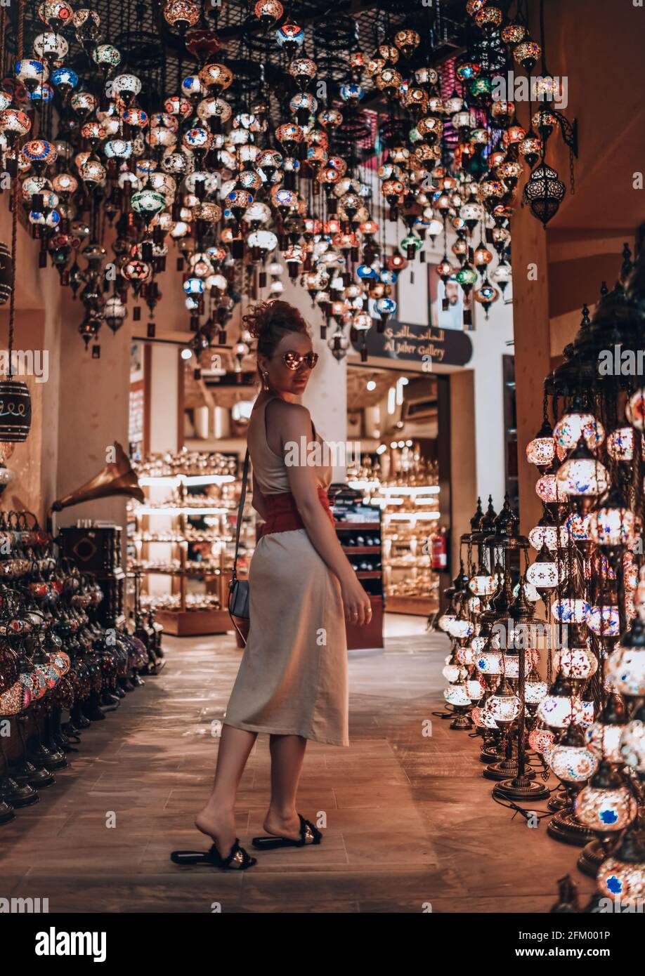 Joyeuse touriste à cheveux rouges en robe d'été aime assister au marché de rue à Dubaï, visiter la boutique de lanternes Banque D'Images