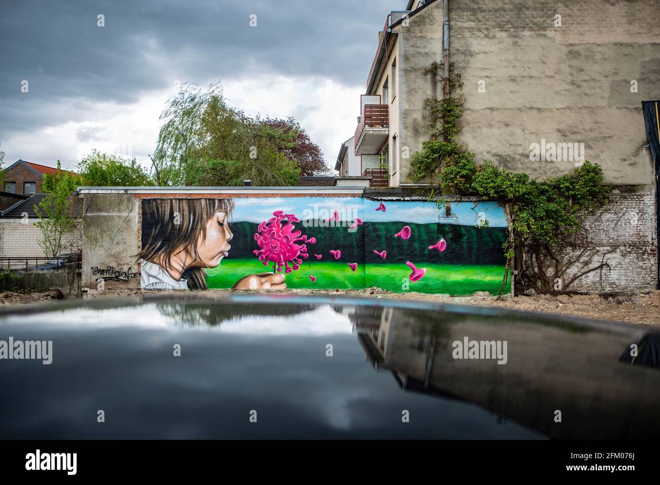 Ein Graffiti an einer alten Mauer zeigt ein Mädchen, welches wie bei einer Pusteblume ein coronavirus anpustet, welches dann auseinander fliegt. Ein s Banque D'Images