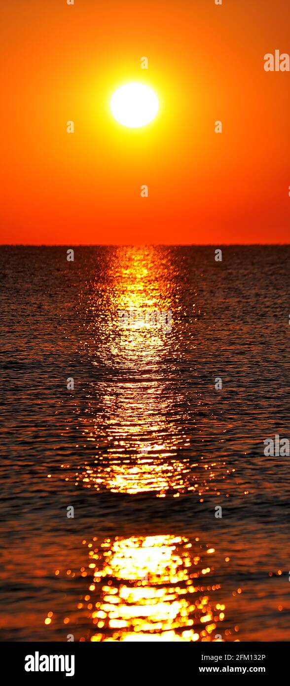 Ciel orangé au coucher du soleil et sentier jaune sur de douces petites vagues de mer. Soirée romantique au coucher du soleil sur la côte Banque D'Images