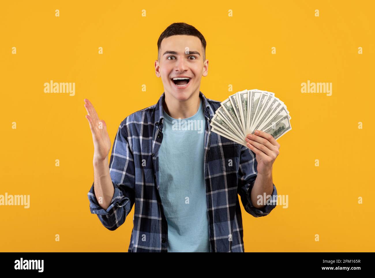 Beau jeune homme heureux de gagner une grosse somme d'argent, détenant des billets en dollars sur fond orange studio Banque D'Images