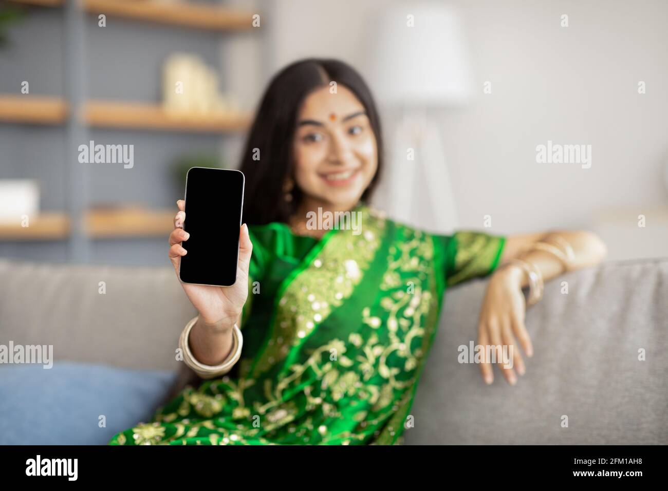Jeune femme indienne dans le pays sari montrant un smartphone avec écran vide à l'appareil photo, maquette pour la conception de site Web Banque D'Images