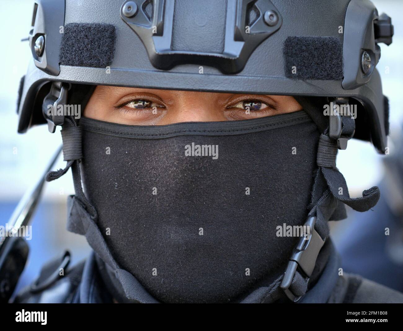 Un jeune officier de police de moto tactique du Caucase porte un équipement de protection personnelle noir avec un casque et un masque facial noir et regarde le spectateur. Banque D'Images