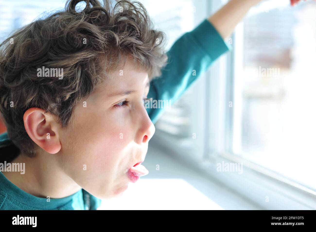 Un petit garçon mignon grimaces à la fenêtre ouverte et bâtons sa langue Banque D'Images