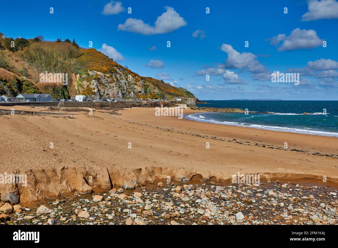 Image de la baie de Greve de Lecq avec le mur du port en arrière-plan, pierres, plage avec une mer bâclée et ciel partiellement nuageux au soleil. Jersey ci Banque D'Images