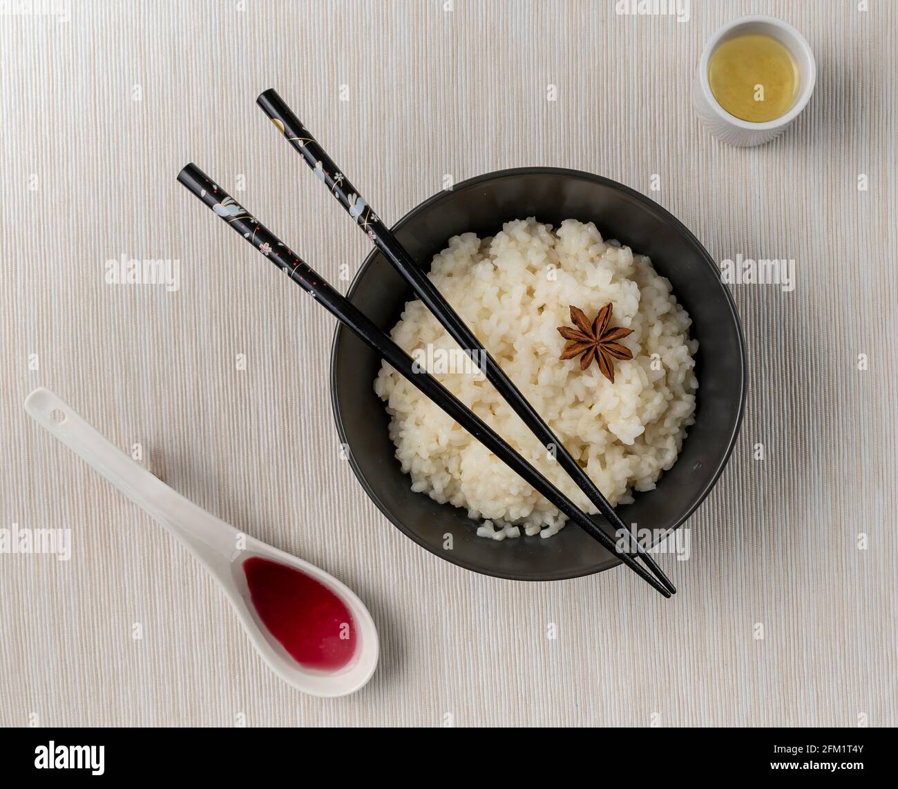 Une assiette de riz blanc avec anis étoilé sur un nappe blanche avec baguettes orientales sur le dessus et à côté c'est un verre de saké et une cuillerée de rouge sauce Banque D'Images