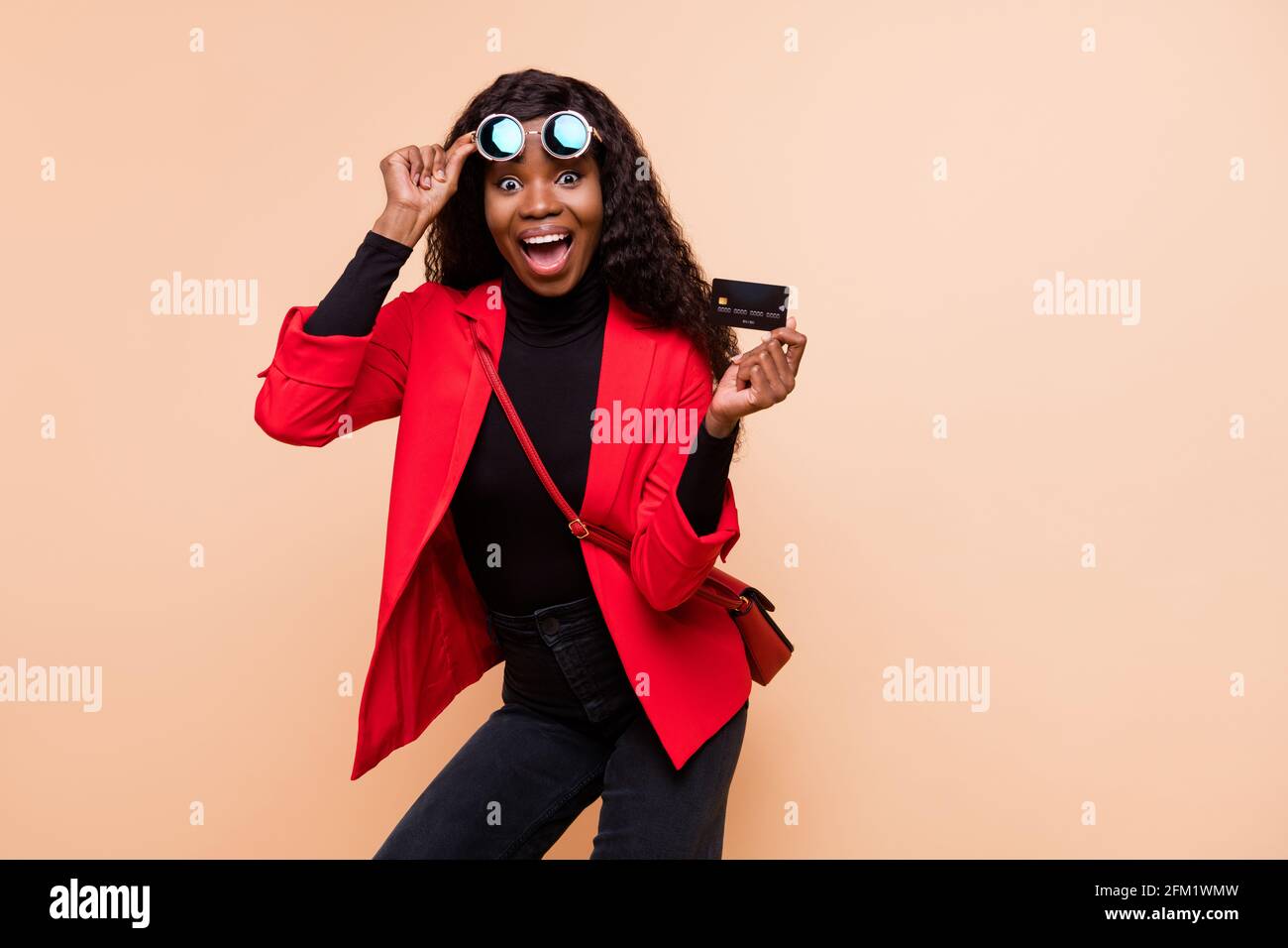 Photo de la femme afro-américaine aux cheveux bruns choqués porter des lunettes tenir la carte de débit isolée sur fond beige Banque D'Images