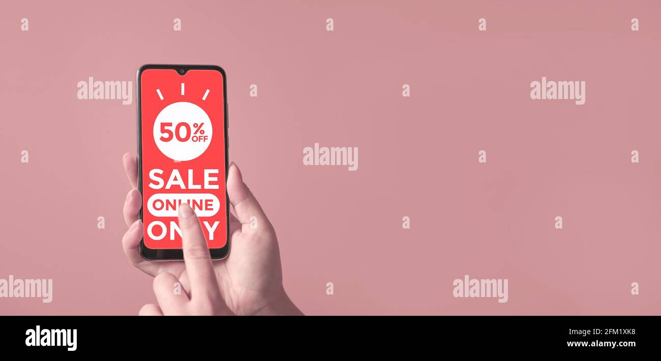 Une femme tient un smartphone avec une affiche de vente en ligne à 50 % sur l'écran sur fond rose. Achat en ligne, concept d'achat par téléphone. Banque D'Images