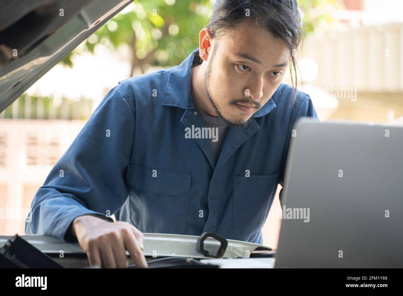 Les hommes effectuant des réparations et diagnostiquées avec un ordinateur portable à l'atelier de réparation automobile. Banque D'Images