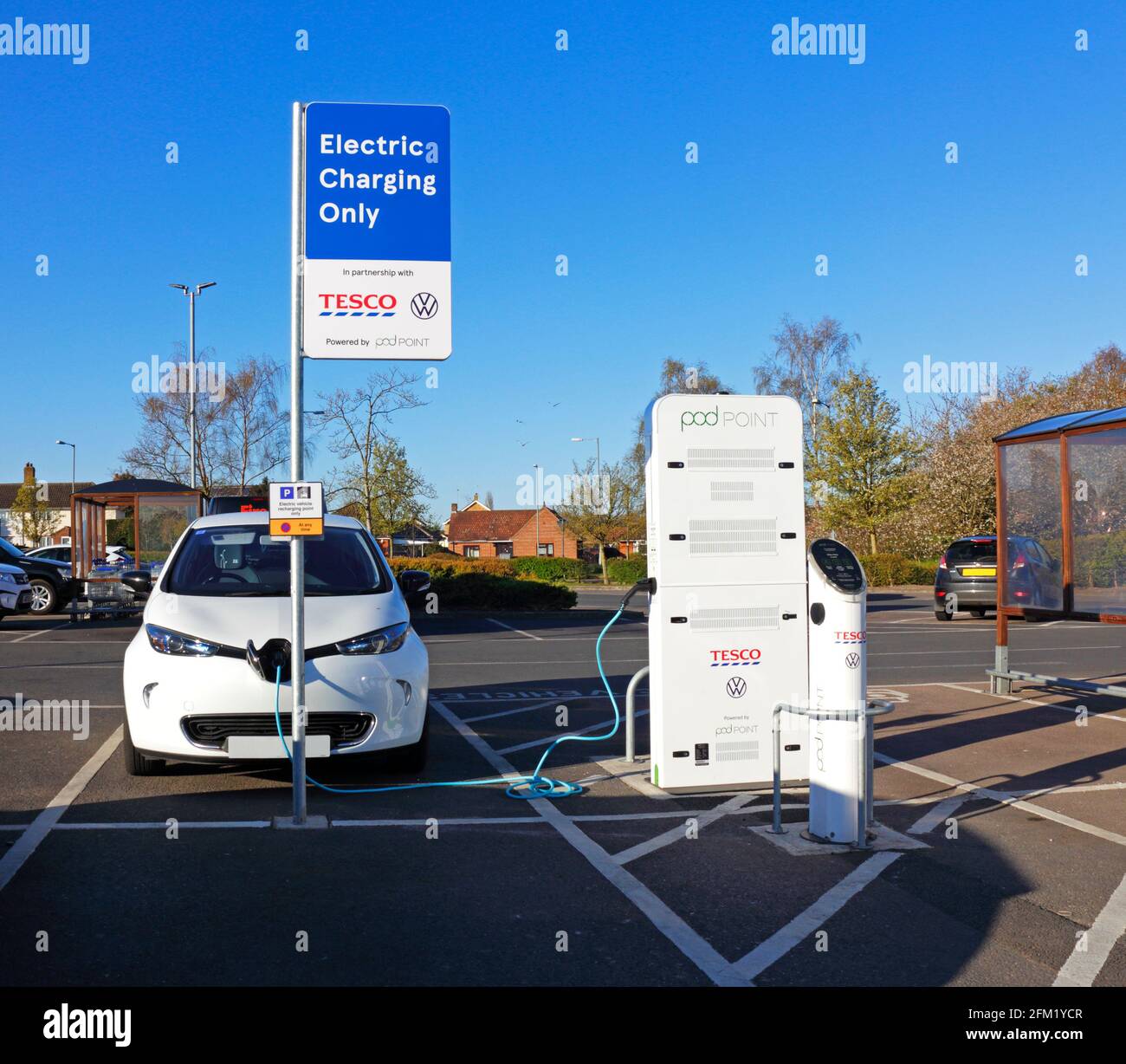 Une voiture électrique reliée à une baie de recharge de point de pod dans un parking de supermarché à Sprowston, Norfolk, Angleterre, Royaume-Uni. Banque D'Images