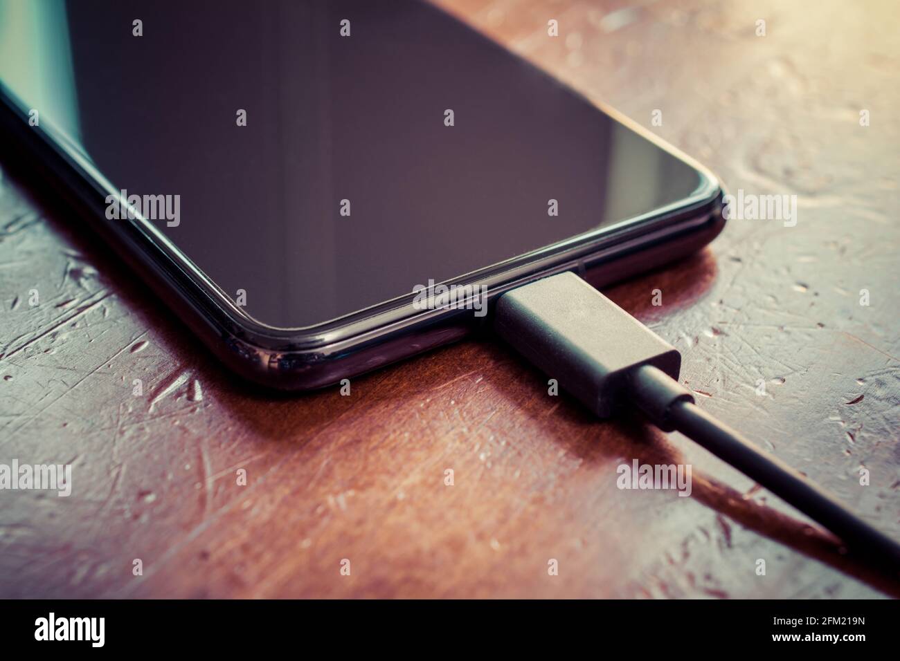 Smartphone noir avec câble USB noir connecté sur UN marron Table en bois Banque D'Images